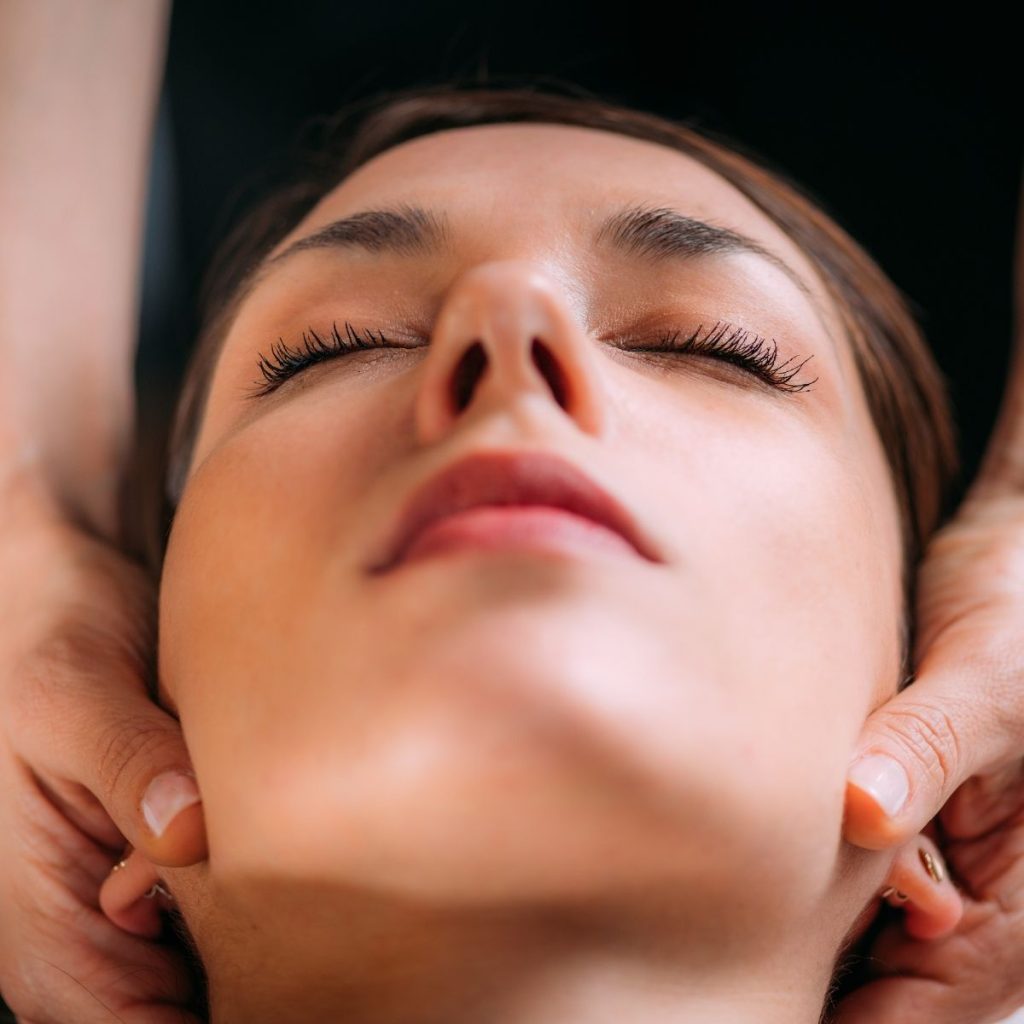 Rostro de una mujer relajada con los ojos cerrados mientras unas manos le trabajan la base del cráneo y la nuca